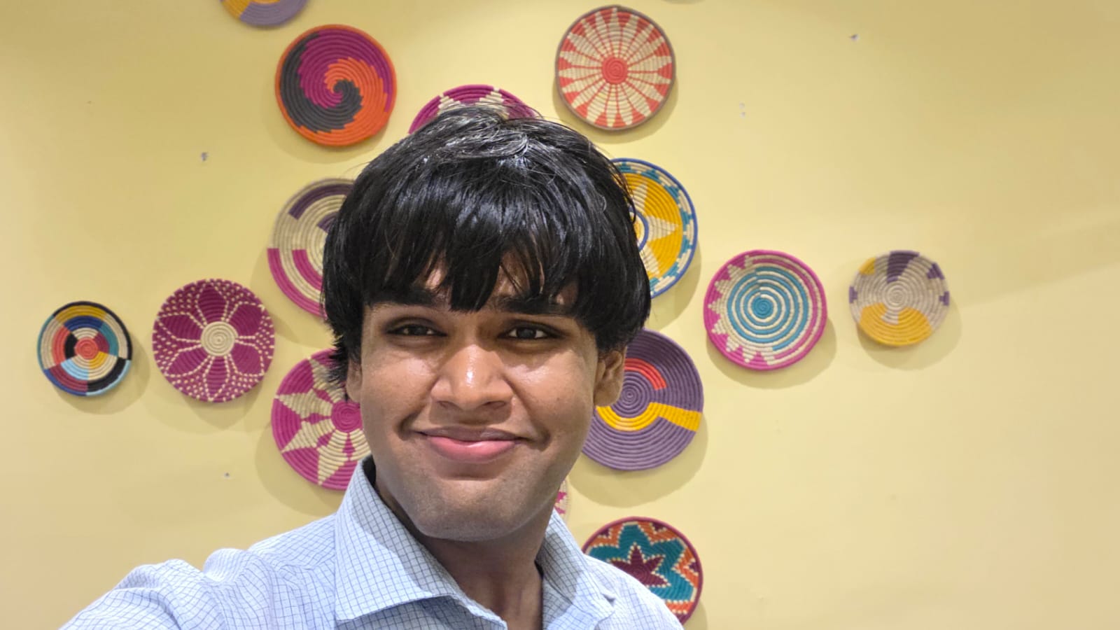 Nitesh at the African Country Culture Centre, in front of colourful woven wall art